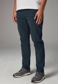 Chinos ajustados de color azul marino con bolsillos laterales y una textura de tela suave. Combinados con zapatillas deportivas grises con detalles en negro.