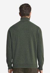 Grön stickad tröja med hög krage och ribbade ärmslut, med en mjuk textur och en något figursydd passform.