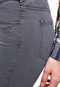 Jeans de mezclilla gris con una textura suave, que cuentan con un bolsillo trasero y un pequeño logo metálico en el bolsillo.