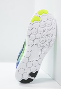 Semelle d'une sneaker dotée d'un motif hexagonal blanc, avec des accents en caoutchouc noir et vert fluo, le tout sur un dessus coloré et texturé.