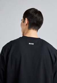 Sort oversized t-shirt lavet af bomuld med rund halsudskæring. Har en lille hvid "MSGN"-logo på ryggen, glat tekstur.