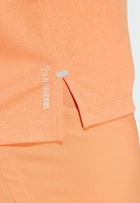 Lys oransje treningsskjorte med sidespalte, med en subtil tekstur og "climacool"-merke i hvitt. Stoffet er glatt og pustende.