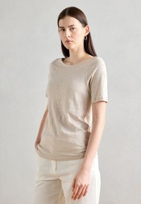 Beige lyhythihainen T-paita pehmeästä kankaasta, jossa on klassinen pyöreä kaula-aukko ja rento malli. Yhdistetty vaaleisiin tekstuurikankaisiin housuihin.