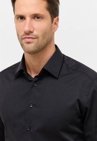Camicia nera con un design strutturato, abbottonatura frontale, colletto punta e texture liscia. Presenta una vestibilità classica e una leggera lucentezza.