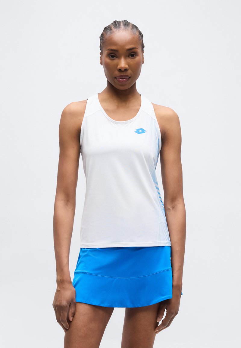 Αθλητική γυναίκα με πλεξούδες, στέκεται μπροστά, φορώντας λευκό αμάνικο τοπ και μπλε αθλητική φούστα σε απλό φόντο.