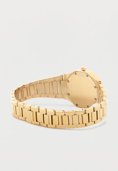 Χρυσό μεταλλικό ρολόι με μπρασελέ από συνδεδεμένους κρίκους, εμφανιζόμενο από πίσω, με την πίσω θήκη και το κούμπωμα πάνω σε λευκή επιφάνεια.