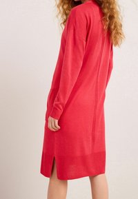 Vestido rojo de punto con mangas largas, escote redondo, aberturas laterales y textura acanalada en los puños y el dobladillo.