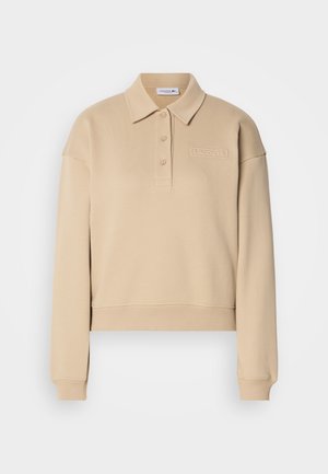 Beige bomullspullover med polo krage, tre knapper, kort design og preget logo på brystet. Myk tekstur og lange ermer.