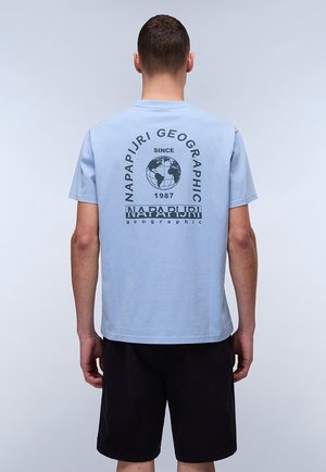 Lyseblå bomulds T-shirt med et trykt globedesign og teksten "NAPAPIJRI GEOGRAPHIC" i sort. Korte ærmer, afslappet pasform, bæres med sorte shorts.