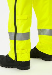 Pantaloni impermeabili ad alta visibilità di colore giallo neon con strisce riflettenti argentate, chiusura con cerniera e rifiniture rinforzate per una maggiore durabilità.