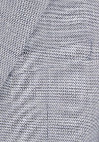 Leichtes gewebtes Material in einem navy- und weißen Pepita-Muster, mit einer strukturierten Oberfläche und einer festen Form.