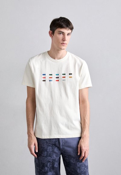 Tricou din bumbac de culoare crem deschis, cu patchuri dreptunghiulare multicolore cu text, guler la baza gâtului și mâneci scurte. Poartă-l cu pantaloni închiși la culoare, cu model.