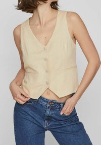 Béžová vesta bez rukávů s hlubokým výstřihem do V, pěti knoflíky a dvěma předními kapsami. Vyrobena z hladké látky, má mírně zkrácený střih.