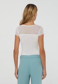 Body bianco a maniche corte con schiena in rete, abbinato a pantaloni azzurri chiari. Tessuto liscio con design aderente e scollatura rotonda.