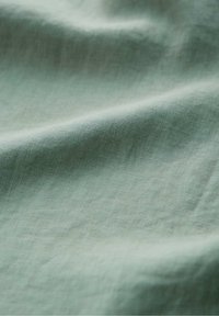 Tissu vert clair et doux avec des plis subtils et une texture finement tissée, créant des ombres douces et une apparence lisse.