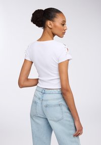 T-shirt bianco aderente con maniche corte e dettagli ritagliati sulle spalle, abbinato a jeans di denim azzurri a vita alta.