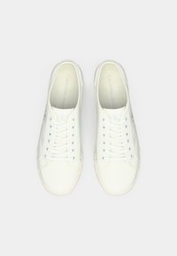 Para białych, niskich sneakersów Calvin Klein Jeans z sznurówkami, widocznych z góry na jednolitym, jasnym tle.