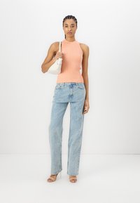 Top a halter a righe di colore corallo, jeans chiari a vita alta con testo stampato e sandali nudi con lacci, abbinati a una borsa a spalla bianca.