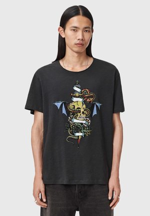 Man met lang zwart haar draagt een zwart T-shirt met een grafische afbeelding van een dolk, schedel, slang, vleermuisvleugels en de tekst "AllSaints".