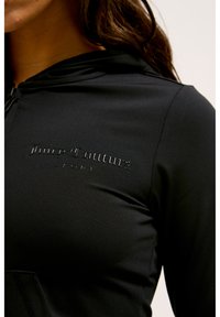 Sweat à capuche noir en tissu lisse, avec un logo ton sur ton en relief "Juicy Couture SPORT" sur le devant.
