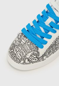 Baskets avec tige en cuir blanc présentant un motif abstrait noir. Les lacets en mesh bleu vif contrastent avec le design. Bout arrondi.