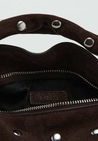 Interior de bolso de ante marrón con bolsillo con cremallera y forro de tela. Detalles de herrajes plateados, etiqueta de la marca visible en el interior.