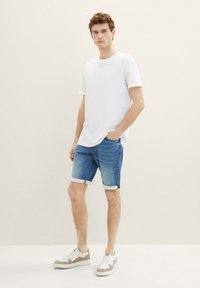 Camiseta blanca de algodón, pantalones cortos de mezclilla azul con puños enrollados y zapatillas blancas con acentos beige. Diseño minimalista y ajuste casual.