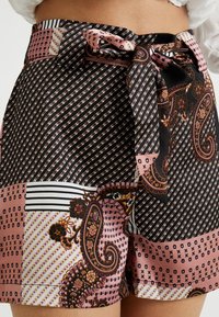Černé šortky se vzorem, které kombinují růžové, bílé a paisley designy. Obsahují zavázání v pase a hladký, lehký materiál.
