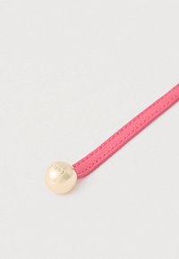 Ružový textúrovaný remienok s hladkým, zaobleným zlatým dekorom nesúcim vyrytý text. Remienok je elegantný a rafinovaný v dizajne.