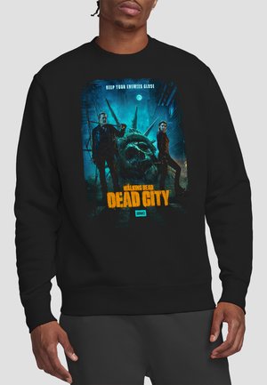 Man wearing black sweatshirt with graphic of two people standing by a broken Statue of Liberty head and text "The Walking Dead Dead City."