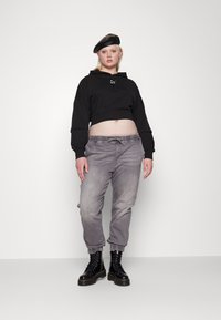 Svart cropped hettegenser med glidelås i front og løse ermer, parret med grå tapered jeans og svarte snøresko. Berett fullfører looken.