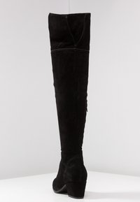 Stivale in suede nero sopra il ginocchio con design affusolato, caratterizzato da un tacco sottile e cuciture visibili lungo la cucitura posteriore.