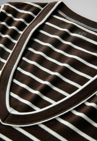 Gros plan sur un tissu marron à rayures horizontales blanches, présentant un col en V côtelé et une texture en maille fine.