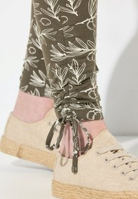 Leggings olive con stampa botanica bianca, arricciati alla caviglia con lacci. Abbinati a espadrillas beige con suola in juta intrecciata e design con lacci.