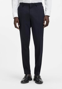 Pantaloni eleganti blu navy con una vestibilità su misura, caratterizzati da una texture liscia, pinces piatte e passanti per cintura. Abbinati a scarpe nere in pelle.