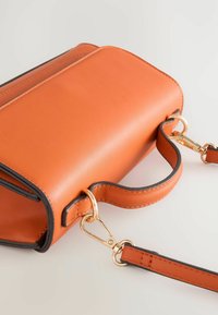 Orange läderväska med en strukturerad form, som har detaljer i guld och en avtagbar rem. Kanterna har svarta accenter för kontrast.