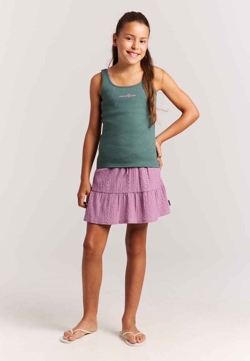 Grünes Tanktop mit Rundhalsausschnitt und besticktem Logo, kombiniert mit einem mehrstufigen, fliederfarbenen Rock mit Ösenmuster und geschwungenem Saum.