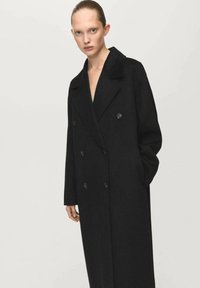 Czarny płaszcz dwurzędowy z wyciętym kołnierzem, długimi rękawami i fakturowaną tkaniną. Posiada długość do połowy uda i dwie przednie kieszenie.