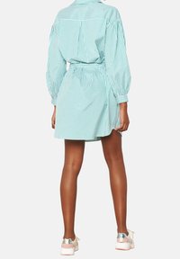 Jasnoniebieska sukienka koszulowa w białe paski z długimi bufiastymi rękawami, paskiem w talii i lekko rozkloszowanym dołem. Połączona z białymi trampkami.