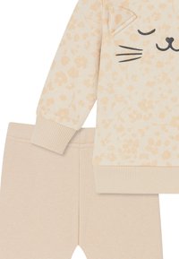 Beige sweatshirt with light tan floral print and cat face design. Matching solid beige leggings feature a simple ribbed waistband.