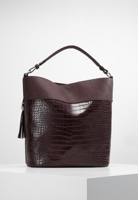 Sac à main en similicuir marron foncé avec une texture crocodile. Présente un bord supérieur incurvé et un détail de gland sur le côté. Poignée solide incluse.