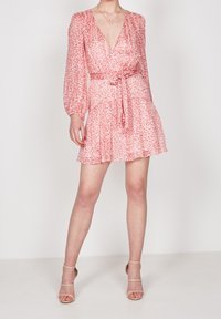 Röd blommönstrad klänning med långa ärmar, V-ringning, åtdragen midja och lagerkjol. Tillverkad av lätt tyg, i kombination med hudfärgade klackar.