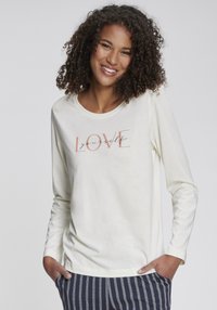 Långärmad krämfärgad topp av mjukt tyg, med ett tryckt motiv "LOVE yourself" i rosa och svart text, ihop med randiga byxor.