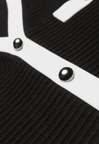 Gros plan sur un tissu noir côtelé avec une bordure blanche présentant deux boutons argentés, brillants et arrondis.