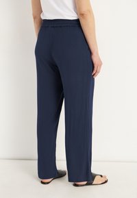 Donkerblauwe gekreukte stof broek met een brede pijpdesign, elastische tailleband en een gladde textuur, gecombineerd met zwarte slidesandalen.