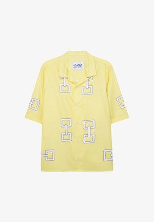 Chemise à manches courtes en tissu jaune vif avec un motif de chaîne géométrique en gris, dotée d'un col et d'une fermeture par bouton.