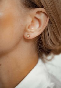 Boucle d'oreille en or avec un petit détail en perle blanche. Forme ronde simple, texture lisse, et conçue pour les oreilles percées.