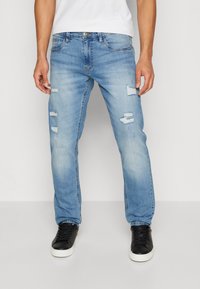 Lyseblå denimjeans med slitte lapper og rett passform. Har fem lommer og glidelås med knapper. Kombinert med svarte joggesko.