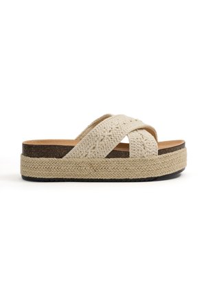 Sandalia tipo slide beige con tiras cruzadas tejidas, plantilla de corcho, entresuela de yute trenzado y suela exterior de goma negra.