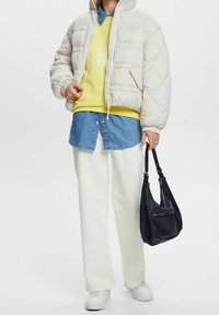 Prošívaná bunda v světle béžové barvě, prošívaný design. Vrstvená se žlutou mikinou a modrou džínovou košilí. Bílé kalhoty s širokými nohavicemi a černá taška přes rameno.